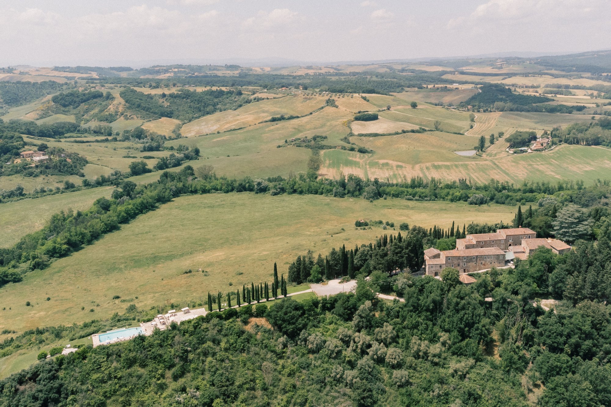 Aerial view of Borgo Laticastelli with its stone buildings, pool, cypress trees and surrounding Tuscan countryside